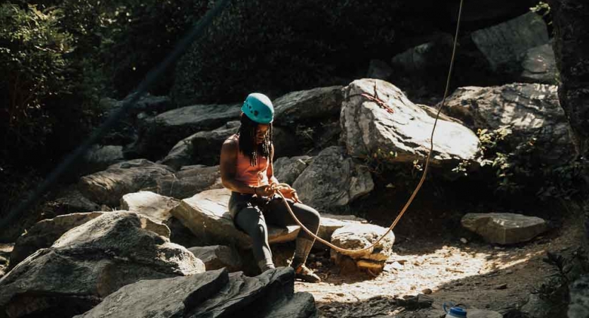 a person wearing rock climbing gear rests on a rock on an outward bound trip for lgbtq teens